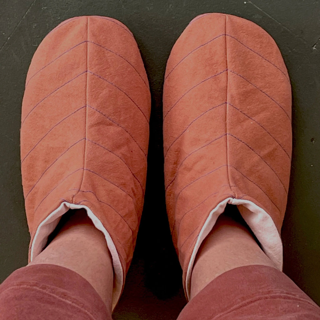 Cozy slipper sewing pattern - Pair of orange quilted slippers on a dark surface