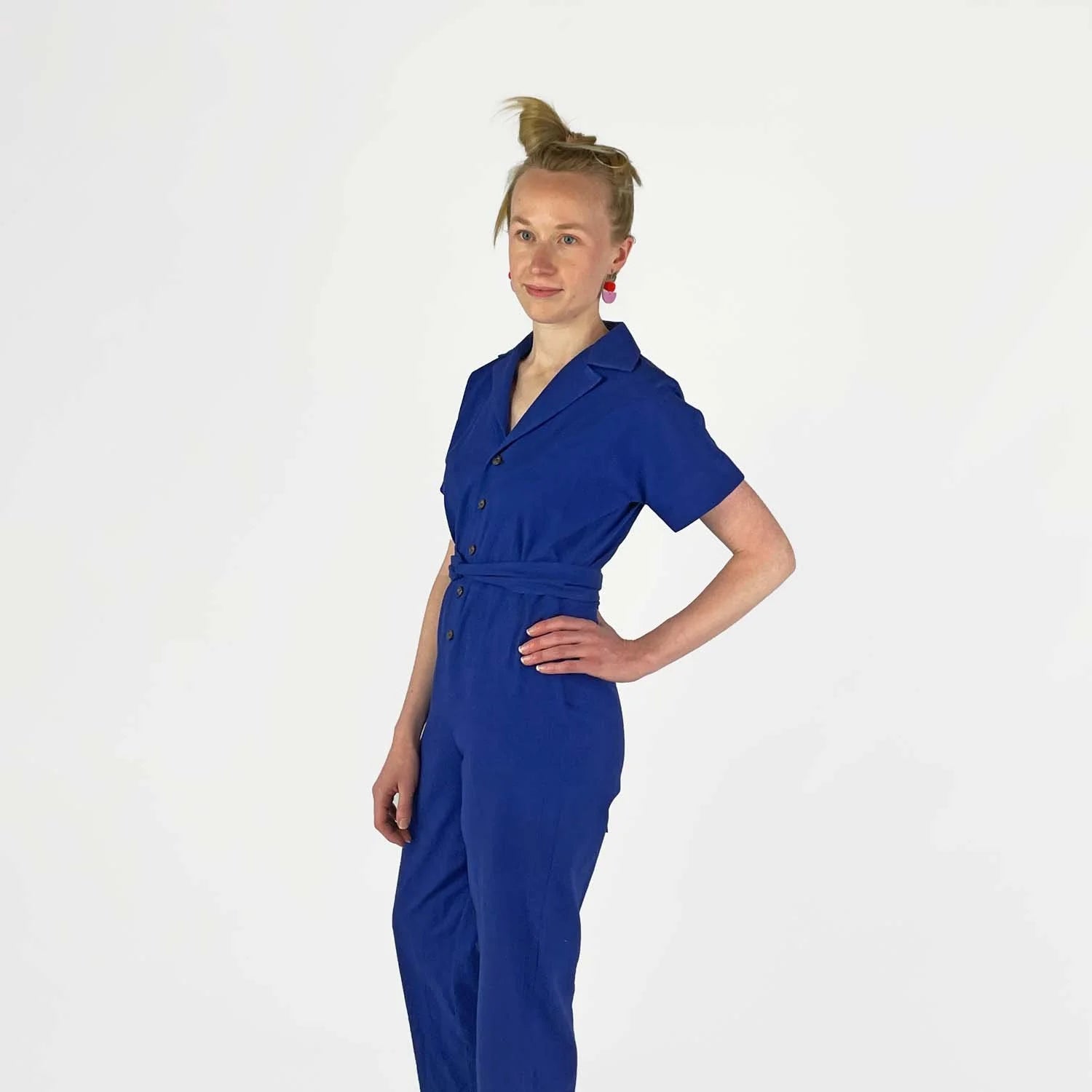Bumper Jumper sewing pattern — woman wearing a loose-fit blue woven jumper with side pockets, front buttons and roll-up sleeves, side view