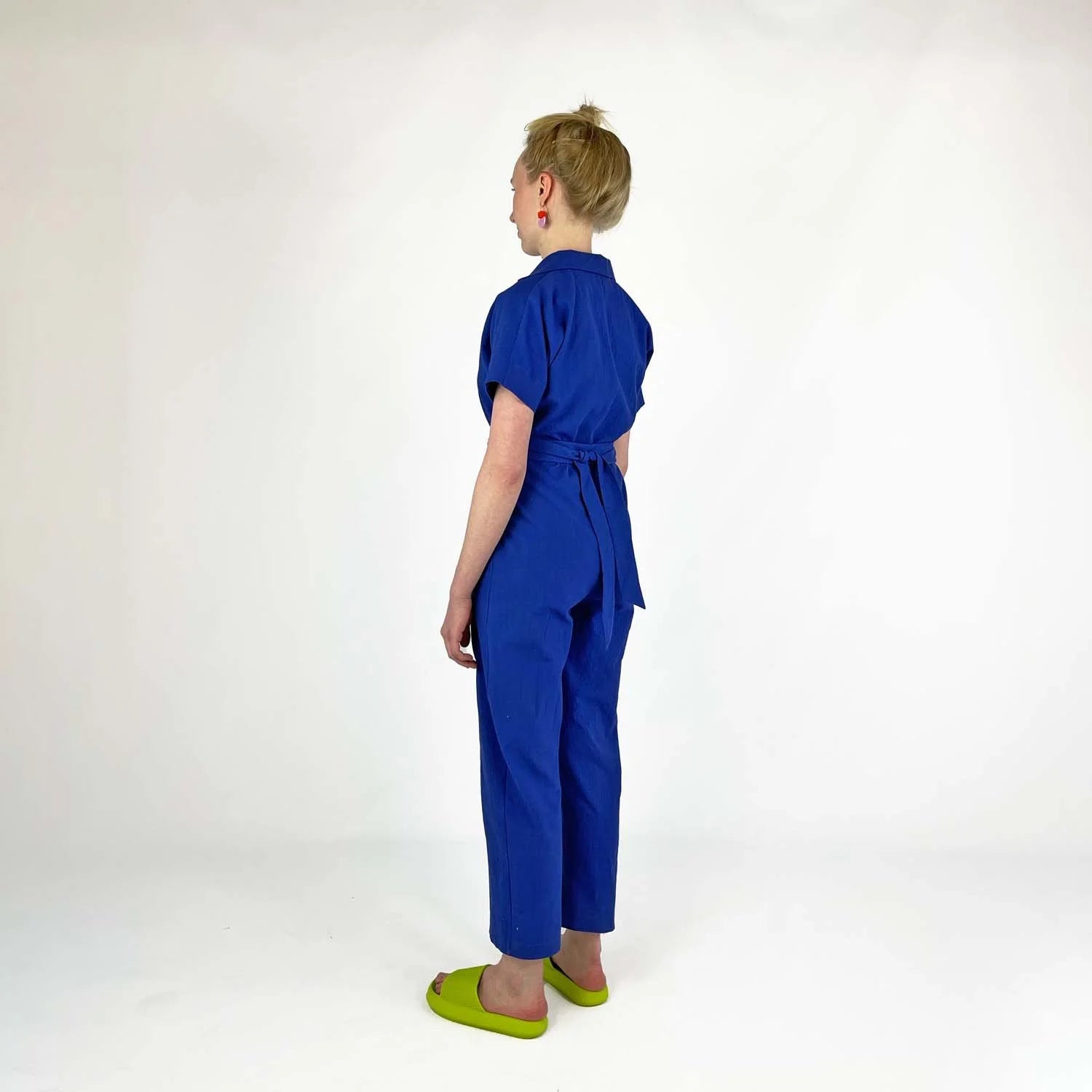 Bumper Jumper sewing pattern — woman wearing a loose-fit blue woven jumper with side pockets, front buttons and roll-up sleeves, back view