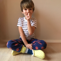Kids Cozy Slipper sewing pattern — child sitting cross-legged wearing handmade slippers in yellow geometric print fabric with grey cuff, front view