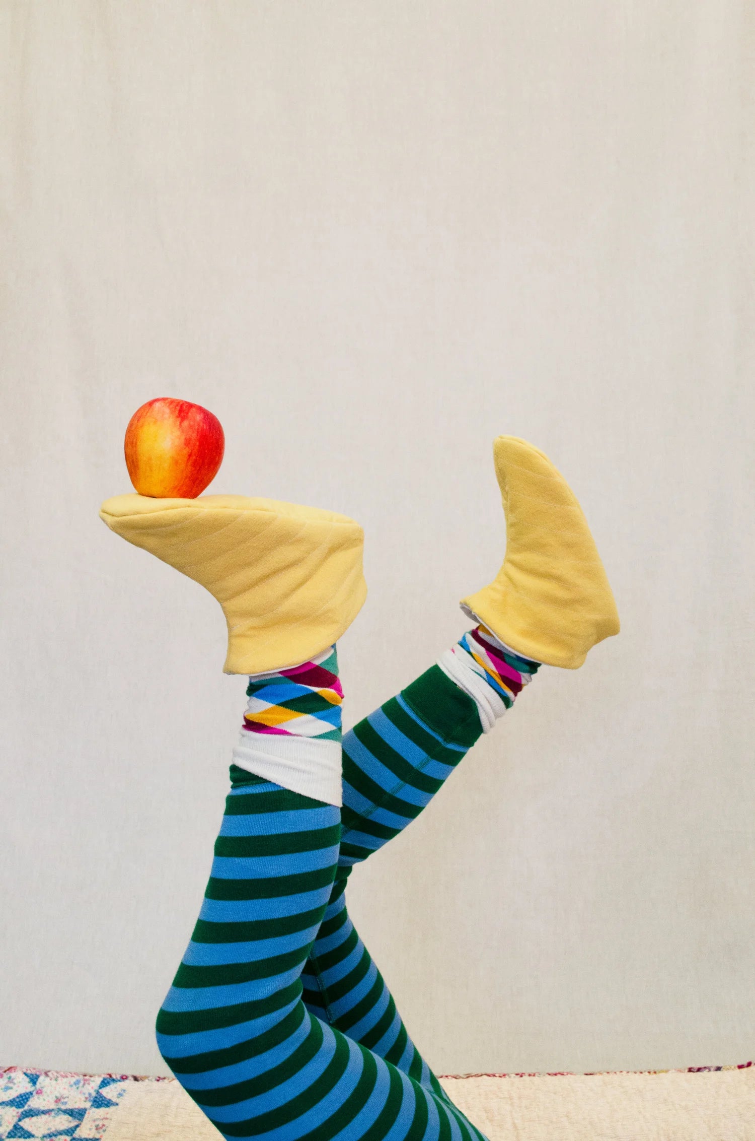 Cozy Slipper sewing pattern in yellow with Colorful striped socks and apples resting on foot