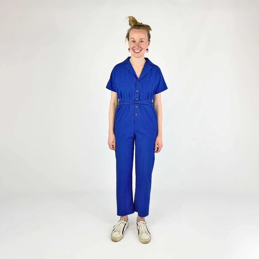 Bumper Bundle sewing pattern — woman wearing a loose-fit woven jumper with side pockets and roll-up sleeves, front view a blue jumpsuit on a white background
