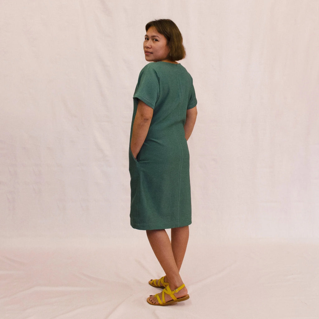 Day Dress sewing pattern — model wearing a relaxed knee-length shift dress in teal linen with scoop neckline, short sleeves, center front seam, and side pockets, back view