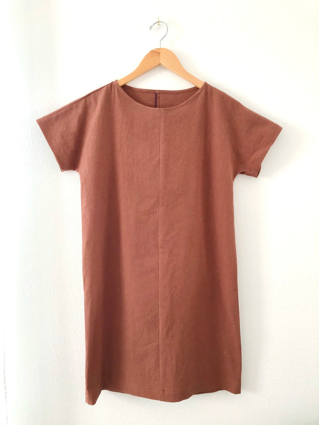 Day Dress sewing pattern — knee-length shift dress in rust colored cotton with scoop neckline, short sleeves, center front seam, and side pockets, hanging view