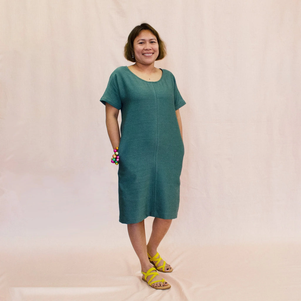 Day Dress sewing pattern — model wearing a relaxed knee-length shift dress in teal linen with scoop neckline, short sleeves, center front seam, and side pockets, front view