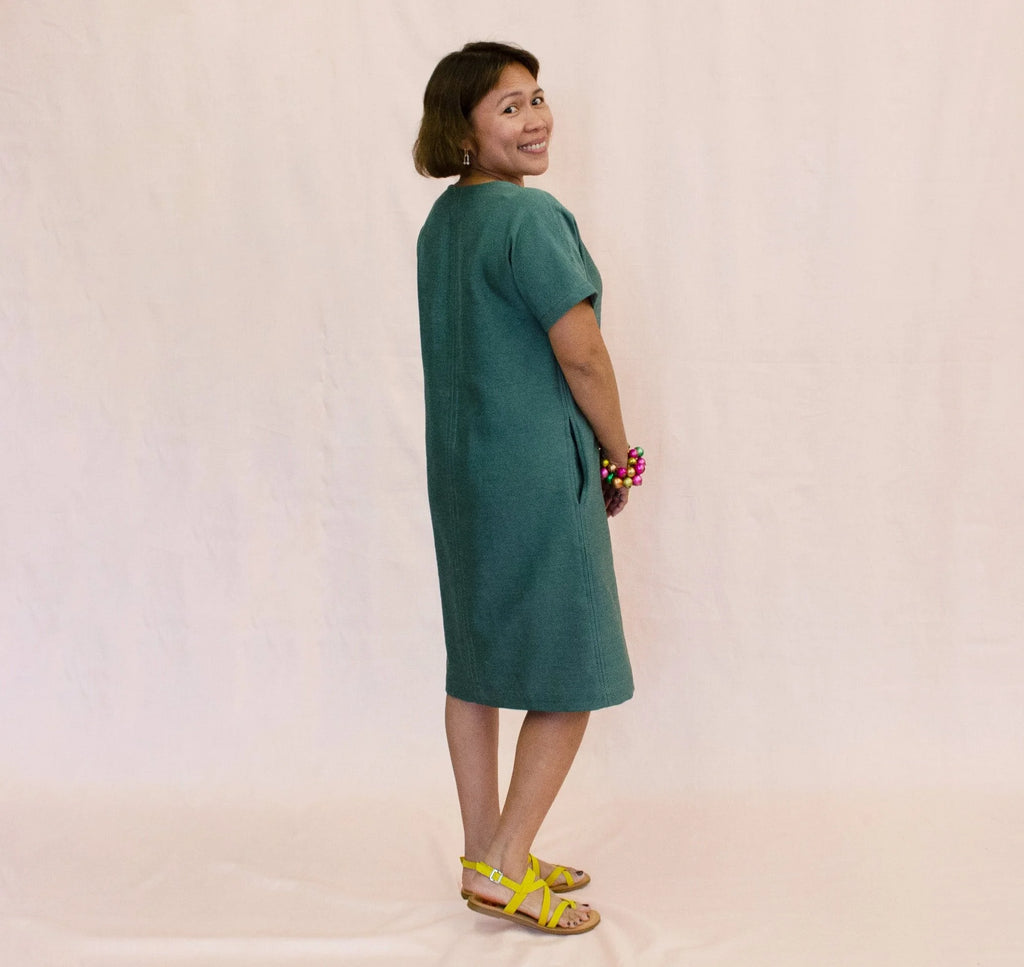 Day Dress sewing pattern — model wearing a relaxed knee-length shift dress in teal linen with scoop neckline, short sleeves, center front seam, and side pockets, side view