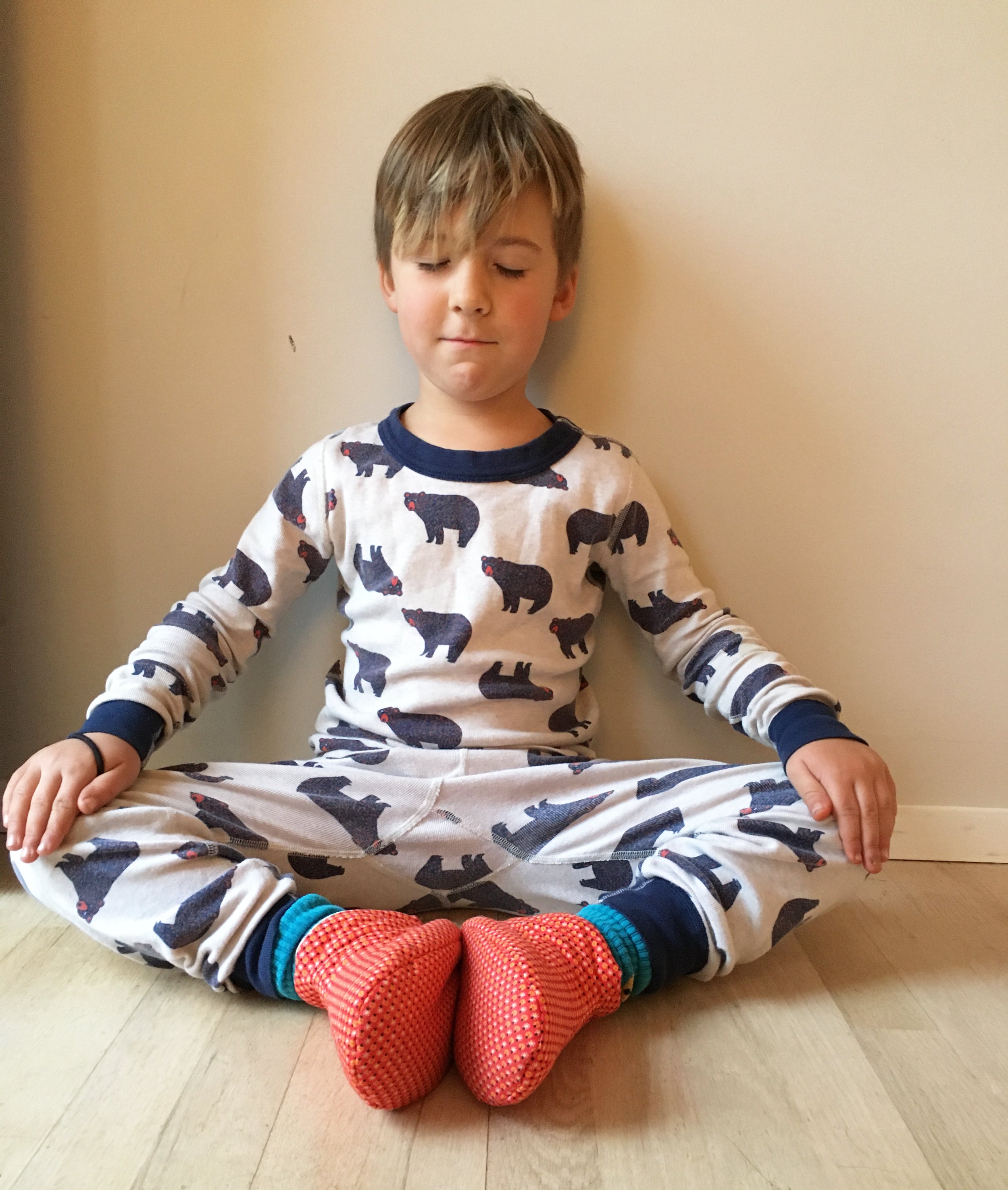 Kids Cozy Slipper sewing pattern — child sitting cross-legged wearing handmade slippers in orange geometric print fabric with grey cuff, front view