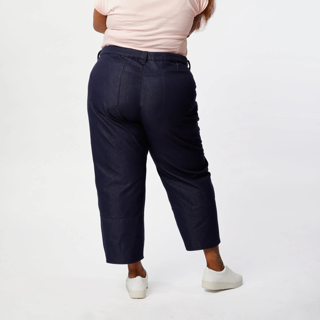 Shop Pant sewing pattern — plus size model wearing high-waisted barrel leg pant in indigo denim twill with front pockets and belt, back view