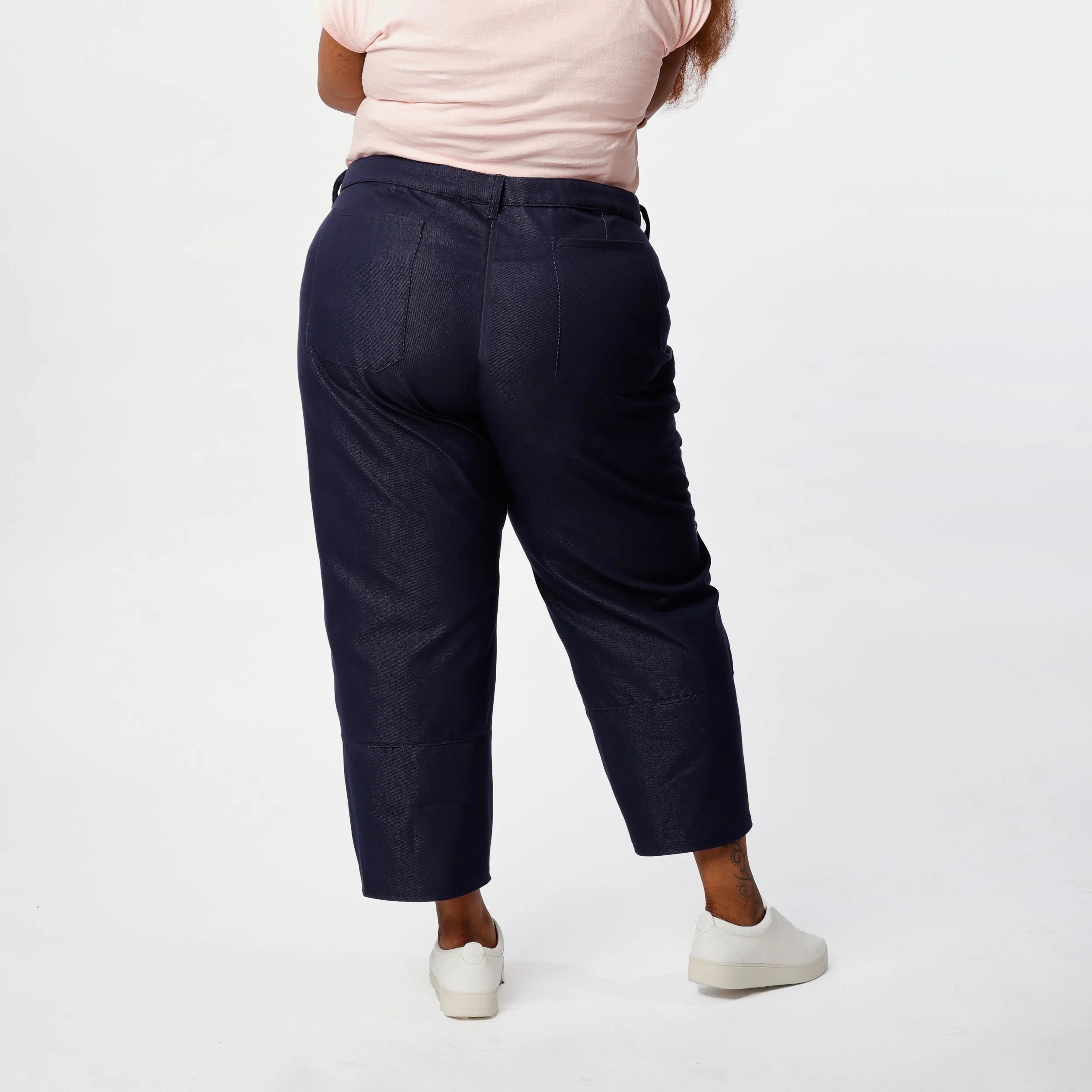 Shop Pant sewing pattern — plus size model wearing high-waisted barrel leg pant in indigo denim twill with front pockets and belt, back view