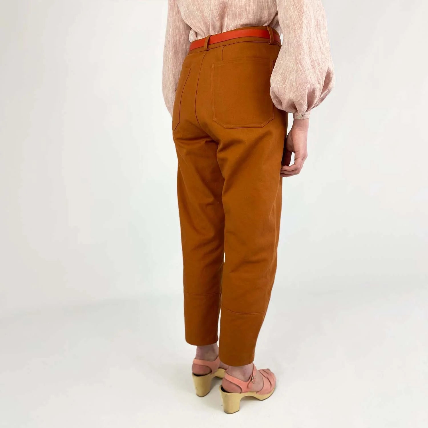 Shop Pant sewing pattern — model wearing high-waisted barrel leg pant in rust brown twill with front pockets and belt, back view