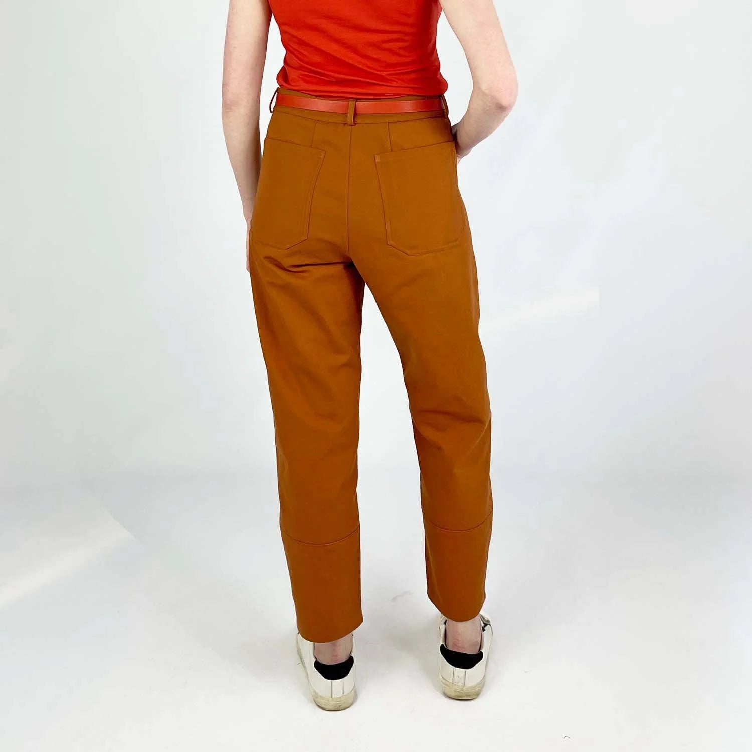 Shop Pant sewing pattern — model wearing high-waisted barrel leg pant in rust brown twill with front pockets and belt, back view
